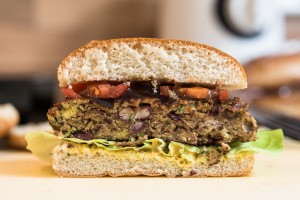 Veggie-Burger auf dem Patty mit Senf, BBQ-Sauce, Salat und Tomaten